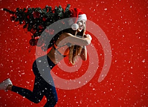 Santa hat Christmas sporting woman holding xmas tree on her shoulders. Winner energy he red background. it`s snowing