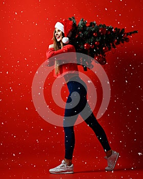 Santa hat Christmas sporting woman holding xmas tree on her shoulders. Winner energy he red background. it`s snowing