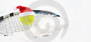 Santa hat on tennis ball on racket on white snow winter background with snowflakes. Merry Christmas and New year concept with