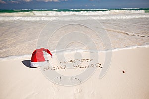 Santa Hat on white sandy beach and Happy New Year