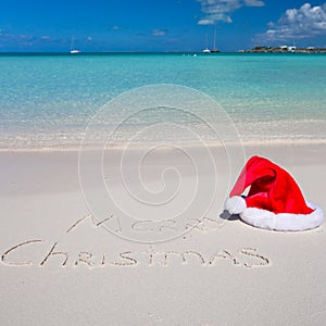 Santa Hat on white sandy beach and Merry Christmas