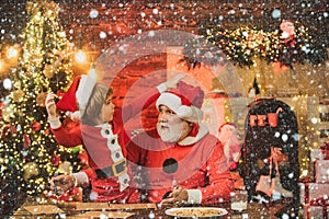 Santa helper. Kid grandson and grandfather in Santa Hat Writing Wish List - unfocused lights background. Child write