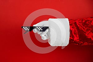 Santa holds funny swag pixilated boss sunglasses on red background. Gangster, Black thug life meme glasses. Pixel 8bit style