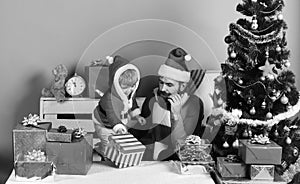 Santa and little assistant among gift boxes near fir tree.