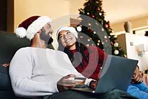 Santa loaned me his credit card. a happy young couple using a laptop and credit card during Christmas at home.