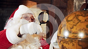 Santa looking into a globe through the magnifying glass.
