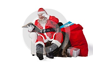Santa reading bible with sack of christmas present beside him