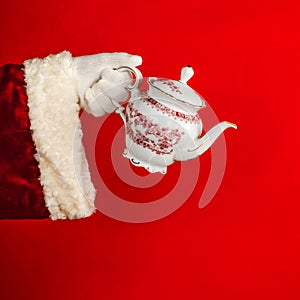 Santa\'s Hand holding porcelain teapot on bright red background with copy space