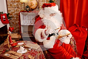 Santa sitting at the Christmas tree, near fireplace and reading a book