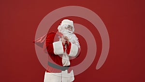 Santa takes a bag with gifts on his back on a red background and leaves the frame. Santa goes to deliver Christmas presents
