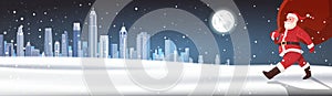 Santa Walking With Big Red Sack With Gifts Over Night Winter City Background Snowy Landscape Horizontal Banner