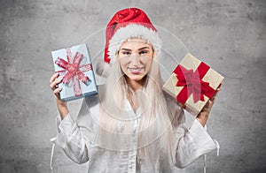 Santa woman holding christmas gifts isolated on gray background. Happy young girl wearing red santa hat and holding present box