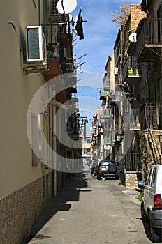 Typical narrow Italian street with old residential houses with many balconies and staircases, parked cars