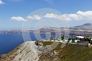 Santorini, Caldera, view of a rocky cliff with a beautiful pool and green palm trees, the sea, in the background a view of