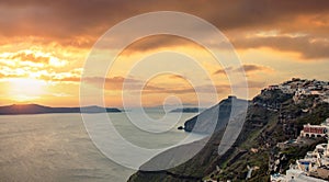 Santorini island, Greece. Fira caldera over Aegean sea, orange color cloudy sky, calm sea