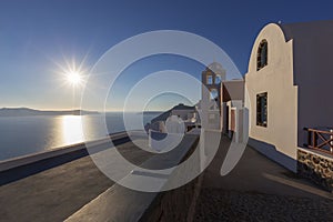 Santorini - picturesque white houses with a white bell tower built at the foot of a cliff falling into the sea. Beautiful sunset