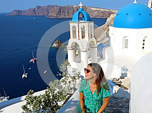 Santorini travel tourist woman visiting Oia, famous white village with blue domes in Greece. Girl in green dress and sunglasses l