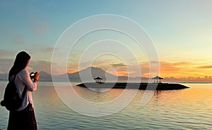 Sanur, Indonesia - April 1, 2019: A young lady standing capturing the sunrise & Mount Agung view early morning at Sanur Beach,