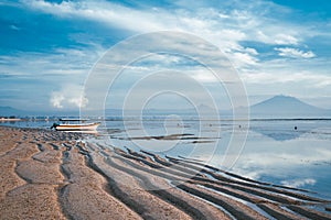 Sanur sandy beach at dawn. Low tide on the beach. Boat at the shore against the background of mountains and a volcano