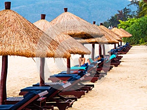 SANYA, CHINA - 4 MAR 2019 - Tourists relax in the tropical sun under straw umbrellas at a beach resort on Hainan Island.