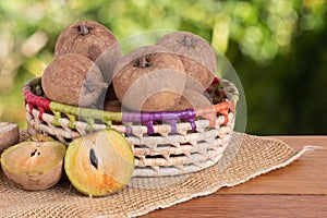 Sapodilla fruit exposed in basket on wooden table with blurred garden background