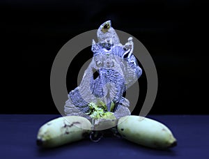 Saraswathi Pooja and Ayudha Pooja Celebrations - Silver idol Murugan with banana on black background.