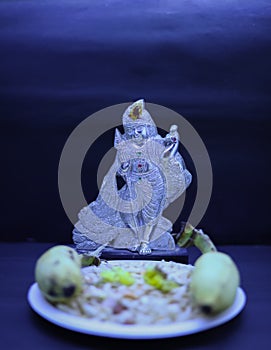 Saraswathi Pooja and Ayudha Pooja Celebrations - Silver idol Murugan with banana, flowers and pori on black background.