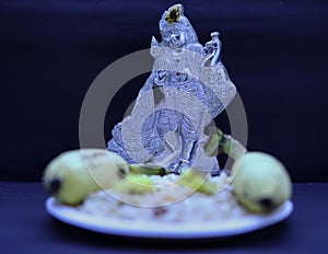 Saraswathi Pooja and Ayudha Pooja Celebrations - Silver idol Murugan with banana, flowers and pori on black background.