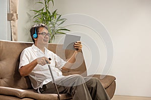 Sarcopenia older man is using digital tablet and headphone on sofa for relax at nursing home photo
