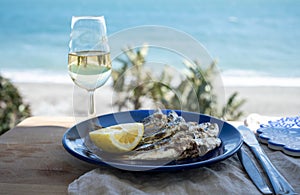 Sardines espeto prepared on skewers and open flame on fireplace with olive trees wood, served outdoor with glass of fino sherry