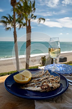 Sardines espeto prepared on skewers and open flame on fireplace with olive trees wood, served outdoor with glass of fino sherry