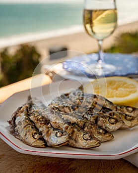 Sardines espeto prepared on skewers and open flame on fireplace with olive trees wood, served outdoor with glass of fino sherry