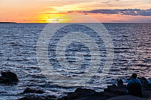 Sardinia.  Portoscuso.  A man sitting on the cliff contemplates the sunset over the sea of â€‹â€‹the Canale di San Pietro