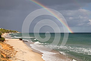 Sardinian coast, rough sea and cloudy sky after the rain with a rainbow that is born on the sea. Rainbow over the sea after a