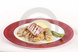 Sarmale,  a traditional Romanian stuffed cabbage dish,  served with polenta,  bacon and hot chilli,  placed on a white and red