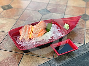 Sashimi in a red plastic bowl on a tile background.