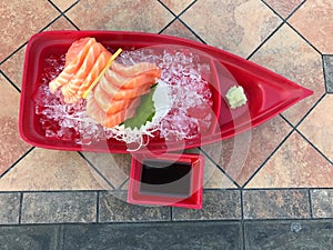 Sashimi in a red plastic bowl on a tile background.