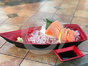 Sashimi in a red plastic bowl on a tile background.