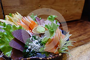 Sashimi salmon and seafood fish in black bowl decoration with vegetable, wasabi on table. Sashimi is something raw, sliced and