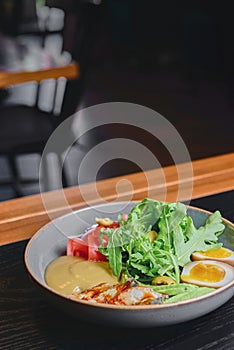 Sashimi Sushi with eel, boiled eggs, avocado, fresh tomatoes and arugula in a plate over black background.