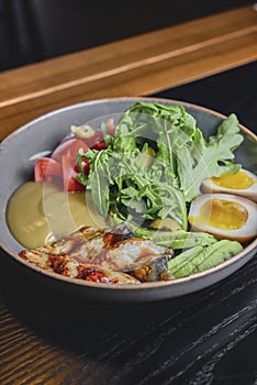 Sashimi Sushi with eel, boiled eggs, avocado, fresh tomatoes and arugula in a plate over black background.