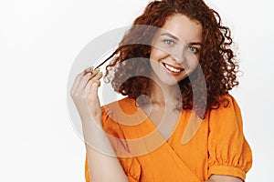 Sassy and beautiful redhead woman with curly short hair, roll curl on finger, giggle and smiling coquettish, flirting