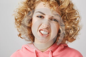 Sassy and classy. Indoor shot of charming joyful woman with natural-looking curls making faces, showing teeth and