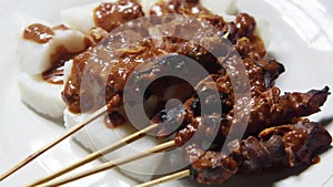 Satay on white plate, served with peanut sauce , rice cake and onion fried