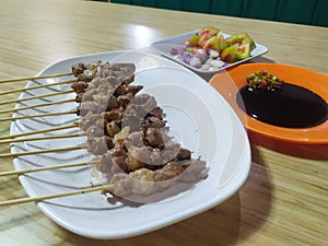 Satay on the white plate with tomatoes red onion and sweet soysauce