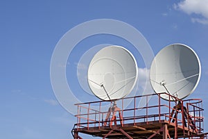 Satellite dish antenna on top of a metal tower against a blue sky