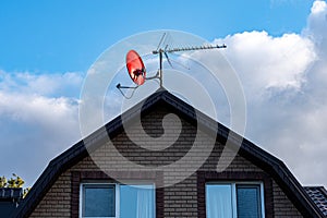 Satellite dish on the roof of a country house against the blue sky and white clouds