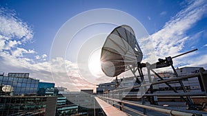 Satellite dish on the rooftop a modern office building, blue sky and setting sun