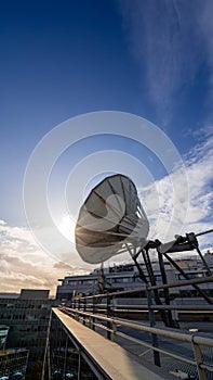 Satellite dish on the rooftop a modern office building, blue sky and setting sun