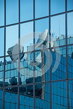 Satellite dishes reflected in the windows of a modern office building